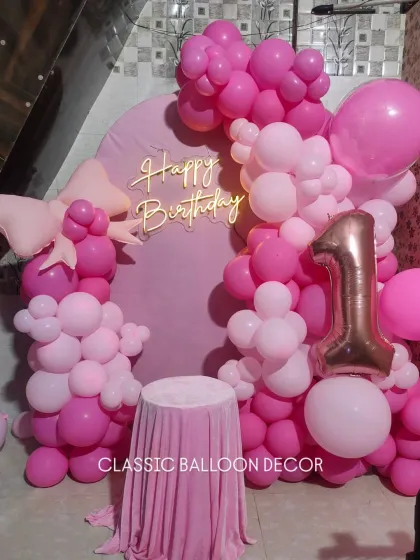 A clear view of the pink arch backdrop and balloon arrangement, highlighting the large bow and number '1' foil balloon.