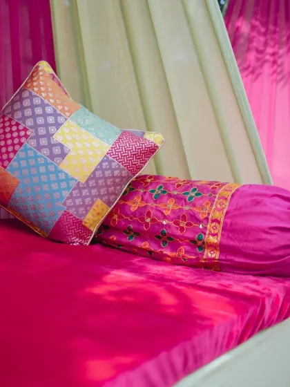 A detail shot of colorful brocade and patchwork cushions on a bright pink seating area, part of a vibrant Mehendi decor theme.