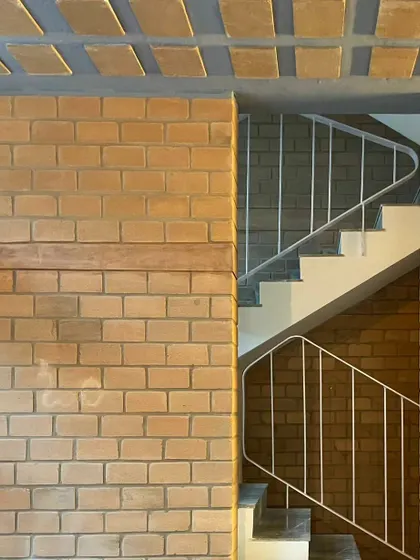 The clean lines of the white metal handrail provide a modern contrast to the rustic texture of the stabilized earth blocks.