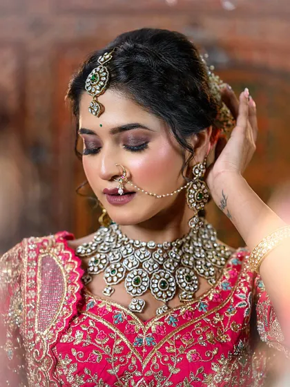 A close-up of a bride in a vibrant pink lehenga. The focus is on her smoky eye makeup and the intricate details of her polki diamond necklace.