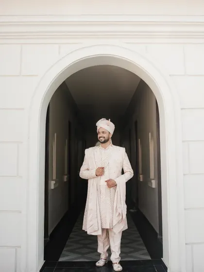 A full-length portrait of the groom in his elegant pastel sherwani, framed by a white archway, exuding calm confidence.