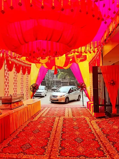 This is a tent setup in a parking area for a housewarming party. The red and yellow theme is carried from the ceiling drapes to the wall panels, and a long buffet counter is set up along the side.