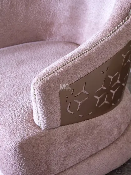 A close-up of the Blush Haven Armchair's antique brass metal accent. This detail shows the intricate geometric pattern and how it wraps around the backrest, adding a touch of modern elegance.