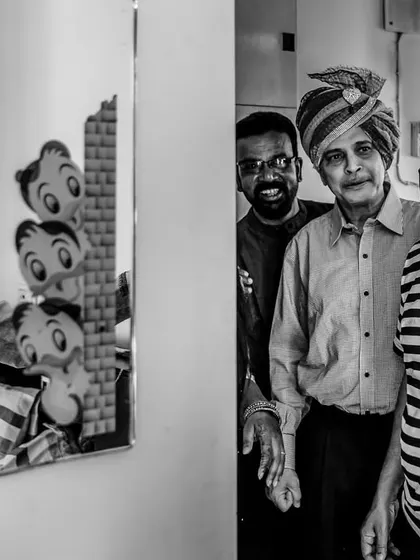 A joyful, candid moment in black and white. The groom looks at his reflection while his smiling father and friends look on, sharing in his happiness.