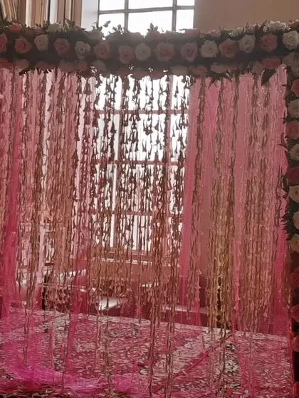 A beautiful mandap or entryway frame decorated with pink roses and a sheer pink curtain with hanging elements, creating a delicate and romantic effect.