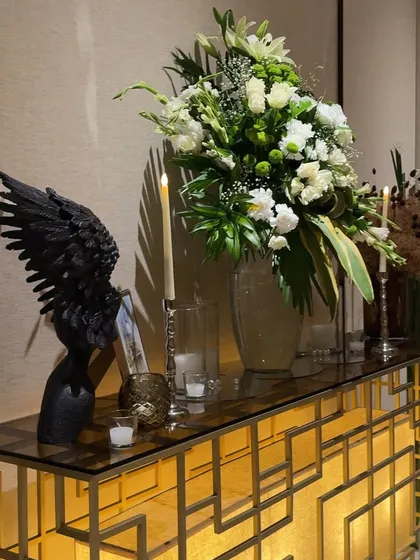 A console table styled with a golden geometric base, a large white floral arrangement, and a dramatic black wing sculpture, blending art with decor.