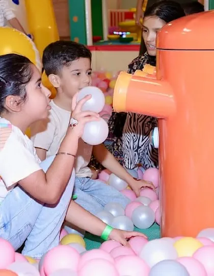 Kids interacting with the ball machine, watching the balls get sucked up and dropped back into the pit.