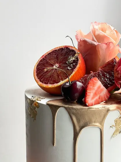 A close up on the gorgeous details of the fruit and floral cake, showing the juicy blood orange, fresh cherries, and delicate gold leaf on the drip.