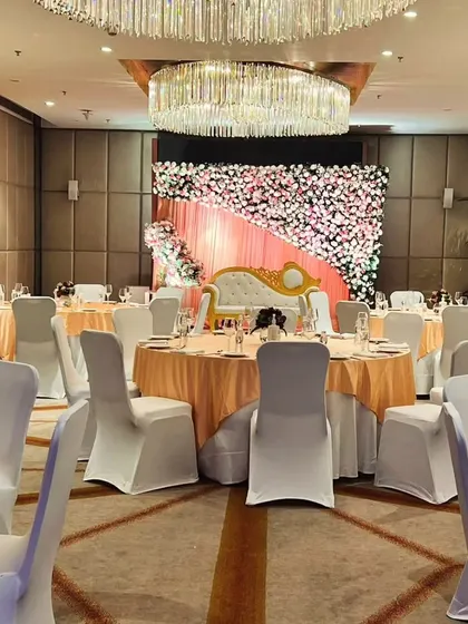 This engagement or reception stage features a full wall of pink and white flowers. The simple yet stunning floral backdrop provides a beautiful setting for photos inside a banquet hall.