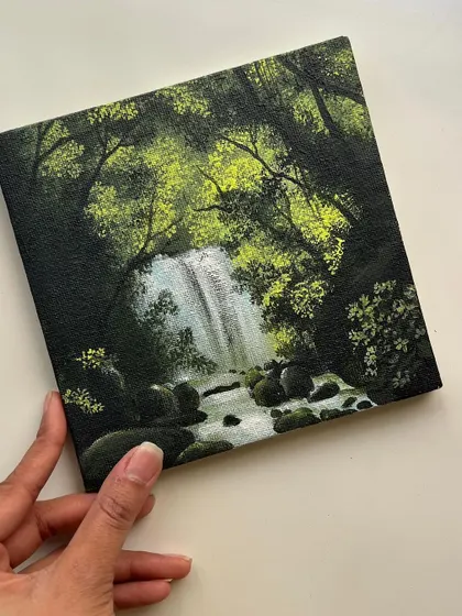 Holding up the finished small canvas of the forest waterfall. It’s amazing how much depth and detail you can create on a small surface with acrylics.