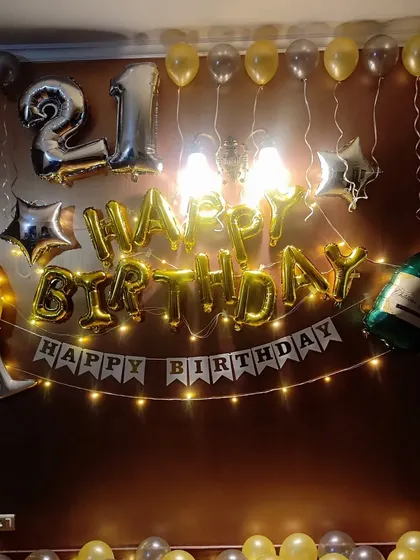 A classic gold and silver setup for a 21st birthday. The decor includes 'Happy Birthday' foil letters, a banner, number balloons, and fairy lights.