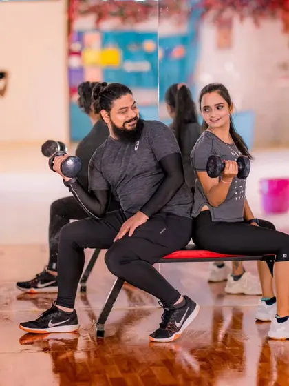 A stylish shot in a gym setting. The couple's coordinated workout gear and the industrial brick background create a cool, modern vibe.