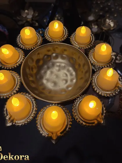 A beautiful urli diya set arranged with ten electric diyas around a central hammered bowl. The warm, flickering light creates a festive ambiance without the hazard of an open flame.