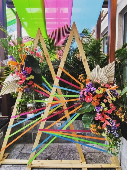 A vibrant photobooth I designed for a 'Colour Pop' themed 50th birthday brunch. The triangular wooden frames are woven with colorful ribbons and accented with tropical flowers to create a joyful and artistic focal point.