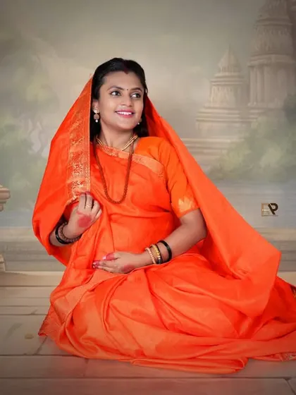 A serene portrait from our Seetha-Ram theme. The mom-to-be looks peaceful and radiant in her orange saree, seated against a backdrop of ancient temples.