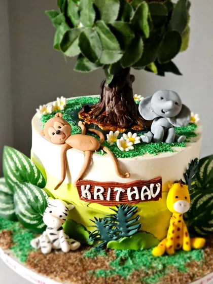 A detail shot of the base of the rotating jungle cake, highlighting the handcrafted monkey, elephant, and giraffe figurines.