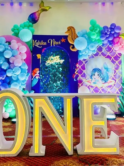 The full stage view of the mermaid first birthday party, featuring a large mermaid tail prop, custom 'ONE' blocks, and a colorful balloon arch.