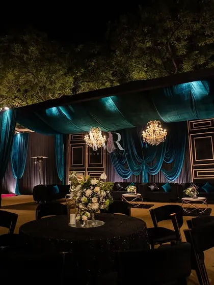 A wider view of the teal velvet lounge area. The gold-framed panels and elegant draping create a sense of an opulent indoor room brought outdoors, complete with sparkling chandeliers.