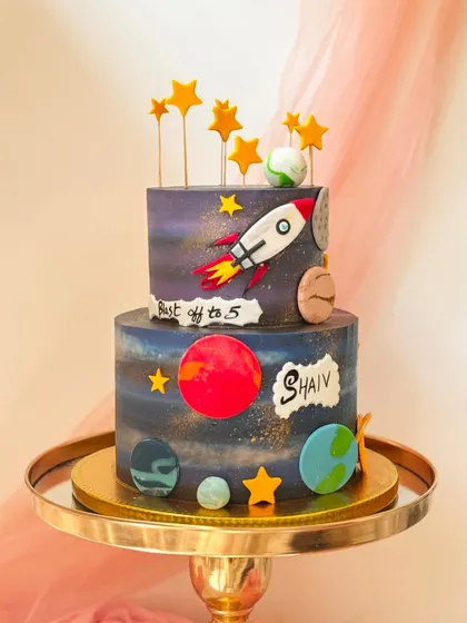 A two-tiered outer space cake that's out of this world. The galaxy-painted buttercream is decorated with planets, stars, and a rocket blasting off.