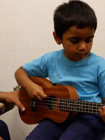 A teacher guiding a young student's hands on the ukulele. We make sure the fundamentals are taught in an encouraging way.