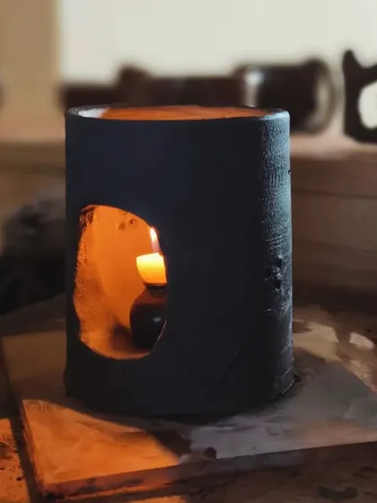 A beautiful, dark-glazed candle holder with a soft, warm glow. This piece was hand-built and carved to create a rustic, organic feel.