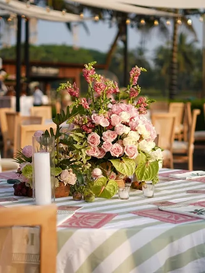The tablescape for this outdoor event featured green and white striped linens, wooden chairs, and beautiful centerpieces of pink and white roses.