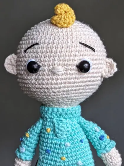 A close-up of the JJ doll's face, showing his curious expression and single yellow curl of hair.