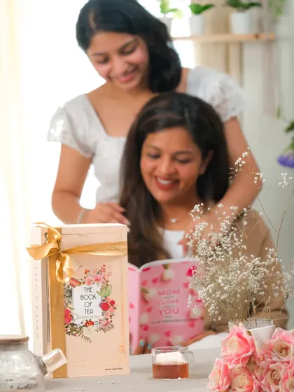 A heartwarming moment between a mother and daughter reading together, with a tea gift box prominently featured.