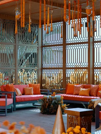 A comfortable and stylish lounge area for a traditional function, with orange sofas and hanging marigold tassels creating a warm and inviting atmosphere.