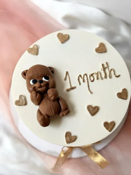 A one-month milestone cake with a 3D sculpted teddy bear and gold hearts.