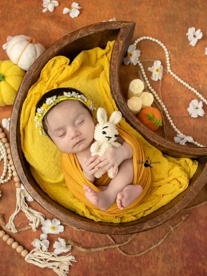 Cradled by the moon. This newborn is sleeping soundly in a wooden moon prop, holding a tiny bunny, part of a whimsical and gentle yellow themed session.