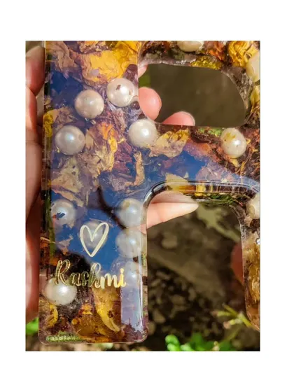 A close-up of a resin name monogram. This letter 'R' is filled with preserved flowers and pearls, with a small, personalized name scripted at the bottom.