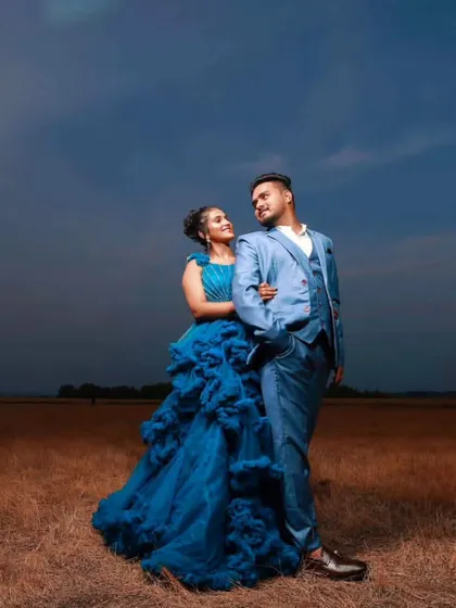 A dramatic, wide-angle shot of a couple in a field. The coordinated blue ruffled gown and three-piece suit create a powerful visual.