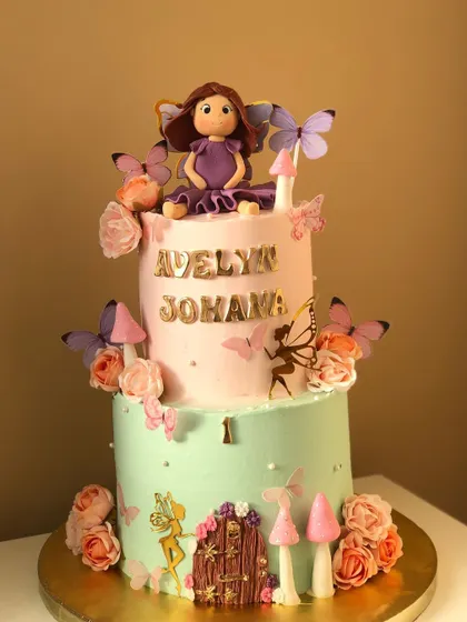 A two-tiered fairy cake for a first birthday, with a pastel color palette and enchanting details like a fairy door and mushrooms.