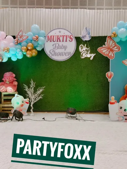 Mukti's baby shower featuring a green hedge wall, a pastel balloon arch, butterfly cutouts, and a neon "Oh Baby" sign.