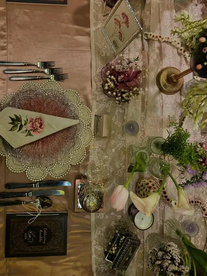 A flat lay of the place setting from Anushka Sharma's birthday dinner. It showcases the custom menu, the delicate floral napkin, and the layered chargers that contributed to the evening's elegant and personal feel.