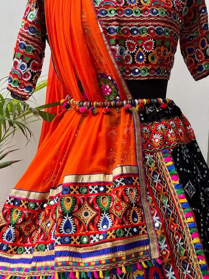 A closer view of the black and orange chaniya choli, focusing on the embroidered waistline and the vibrant orange dupatta.