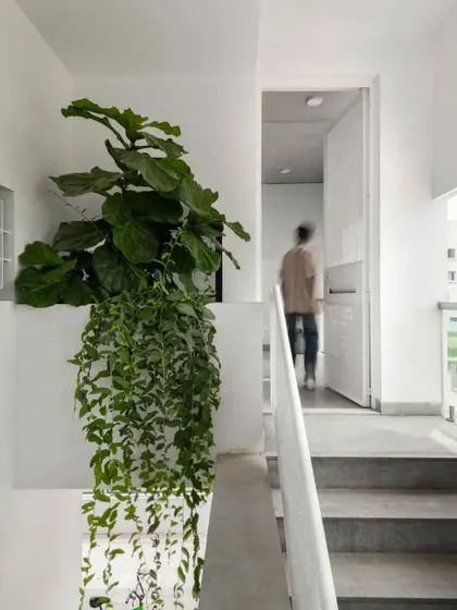 A person walks through the upper floor corridor, demonstrating the human scale of the space. The minimalist design with white walls and simple railings keeps the focus on the home's spatial quality and light.