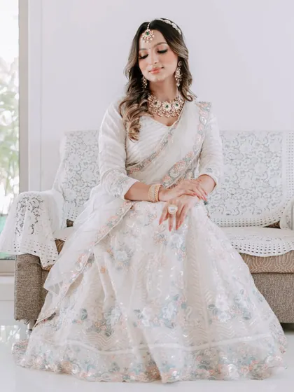 A full-length shot of the model seated, showcasing the delicate floral embroidery on this white rental lehenga.