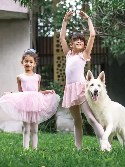 Two graceful ballet dancers pose with one of their Swiss Shepherds in a lovely garden setting.