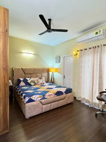 A bedroom from the Sohna Road project, featuring warm wooden flooring, a full-length wooden wardrobe, and a simple, comfortable bed setup.