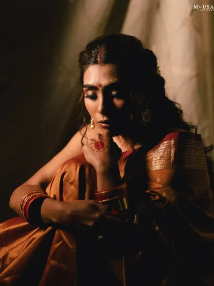 A moody portrait with dramatic shadows. The light falls on the model's face, highlighting her thoughtful expression and the rich colors of her saree.