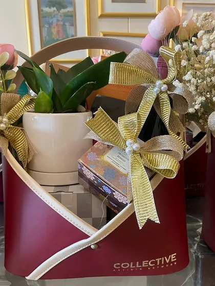 Corporate gifting doesn't have to be boring. This hamper, designed for a corporate client, includes a live plant, a bottle of wine, and other treats in a stylish, modern red container with their branding.