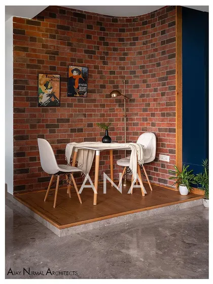 The breakfast deck in Apartment 704, featuring a curved raw brick wall. This cozy nook provides a distinct dining experience, separated from the main living area by a change in flooring level.
