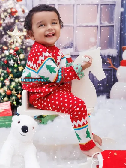 A happy toddler in a Christmas sweater, smiling brightly while riding a rocking horse in a winter wonderland.
