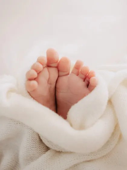A close-up of a newborn's perfect little feet, peeking out from a soft, white knitted blanket. An image of pure innocence.