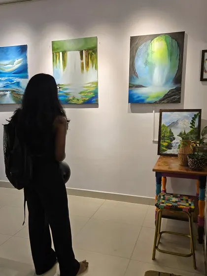 A guest at Gurpreet Kaur's solo show admires a series of serene, abstract waterfall paintings, showcasing the tranquil mood of the exhibition.