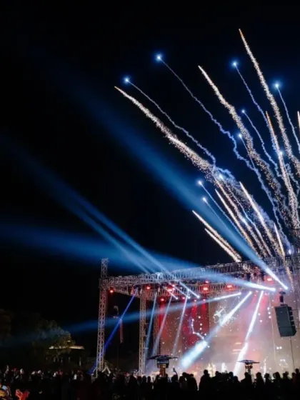 A wide shot of the sangeet, showing the crowd enjoying the concert under a sky lit by fireworks. We aim to create a complete experience that combines music, decor, and spectacular effects.
