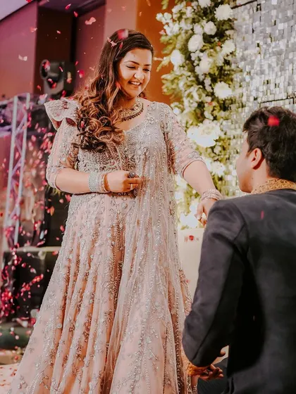 The moment of the proposal. The groom is on one knee as confetti falls around them, capturing the peak emotional moment of the engagement ceremony.