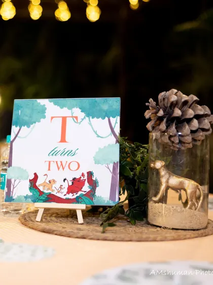 A centerpiece from the twins' "TWO" wild party, with a custom-printed card, a pinecone, and a golden animal figure, combining thematic elements with rustic charm.